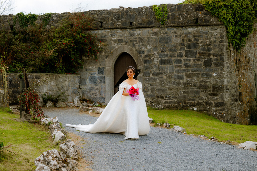bride holding her red bouquet of lfowers walking to the ceremony dressed in white