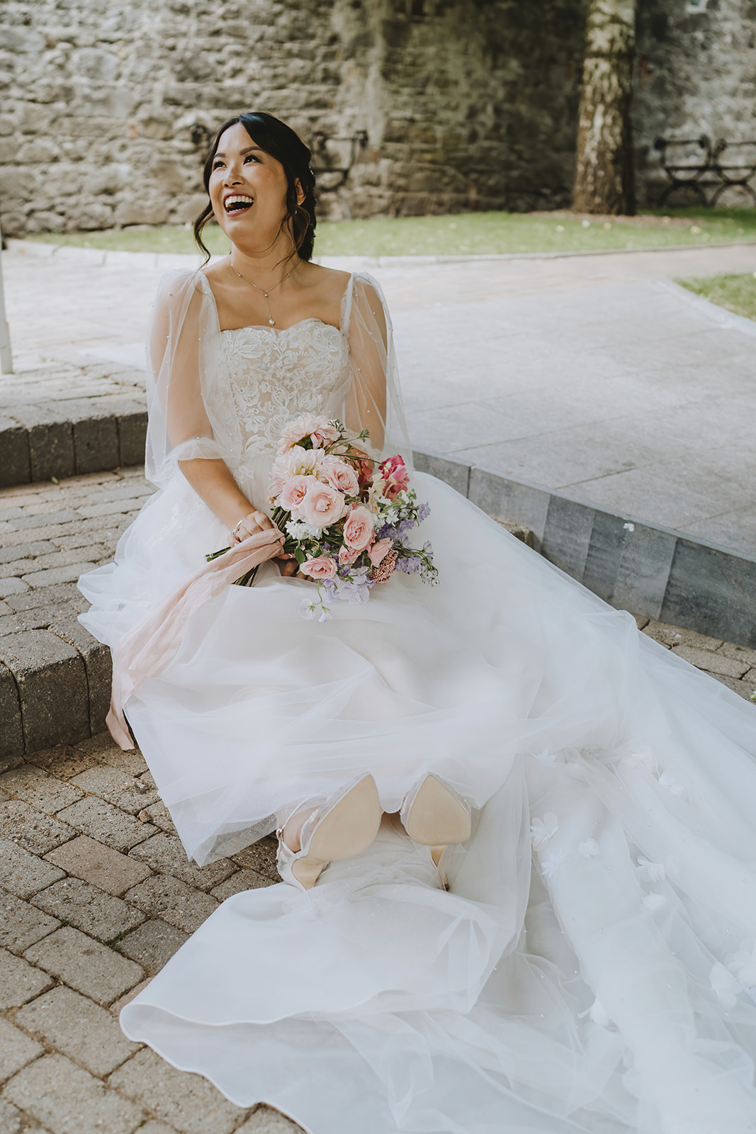 bride with her bouquet and and sitting down on the ground smiling