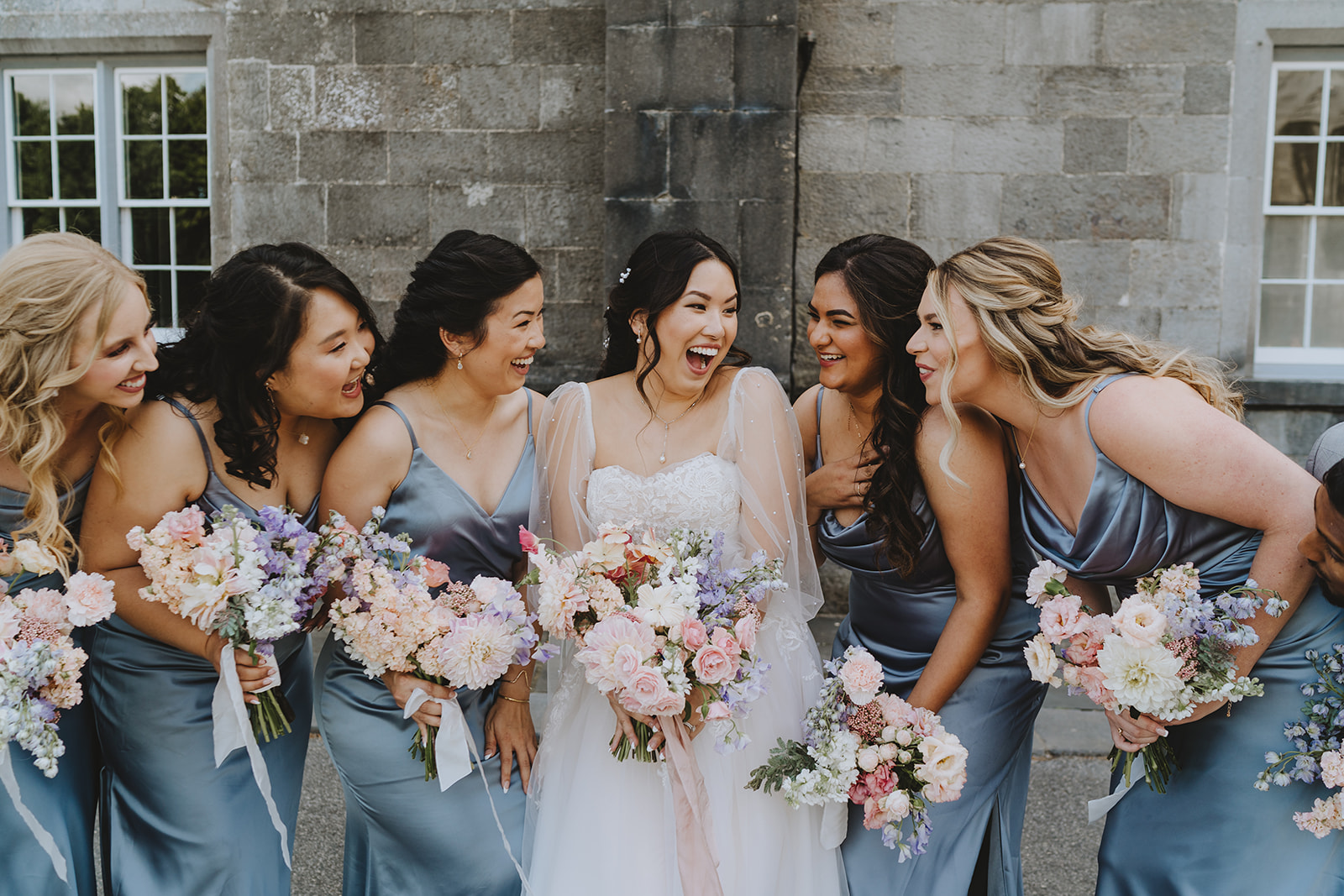 bride Kami with all her bridesmaids smiling with their bridal bouquets