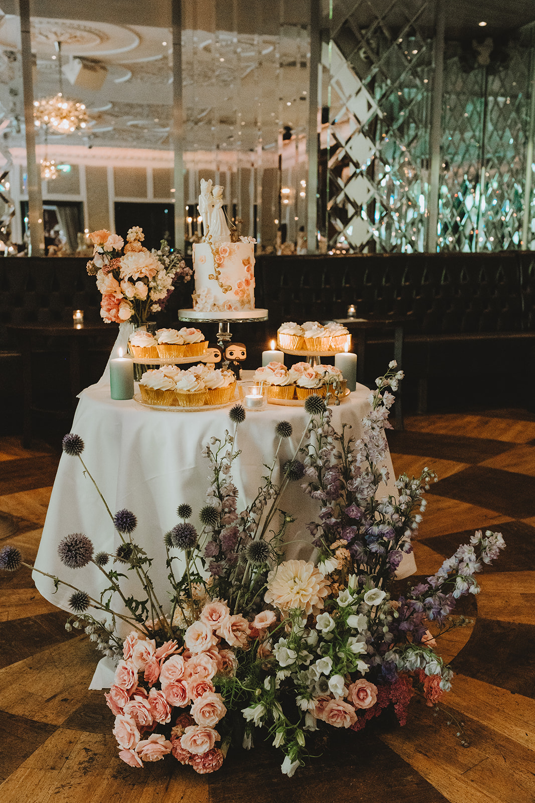 the sweet table with cupcakes and the wedding cake lit with candles and and floral display infront