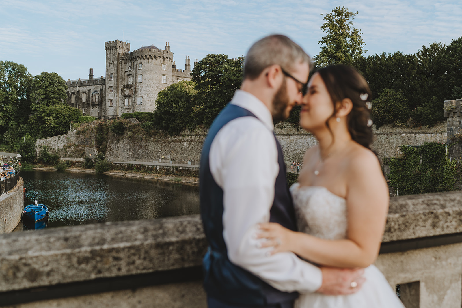 bride and groom kissing with kilkenney castle in the background and blue blota to the left in the water